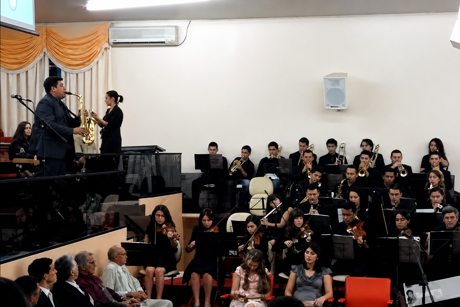 Atrios Orquestra em apresentação em auditório com regente e conjunto completo